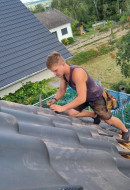 talentierter Dachdeckergeselle bei der Befestigung der Ortgangpfanne auf einem Steildach