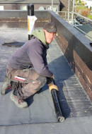talentierter Dachdecker bei Abdichtungsarbeiten mit einer Bitumenbahn auf dem Flachdach